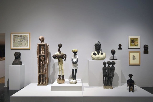 Installationsansicht mit Skulpturen von Dr. Charles Smith, ausgestellt bei Intuit: The Center for Intuitive and Outsider Art, Chicago, im Hintergrund Werke von Henry Darger und William Dawson